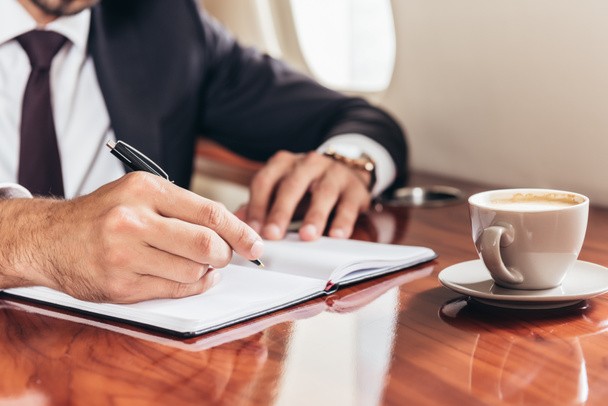 cropped view of businessman writing in notebook in private plane  - Photo, Image