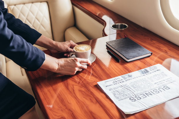 cropped view of flight attendant putting cup of coffee on table in private plane  - Fotó, kép