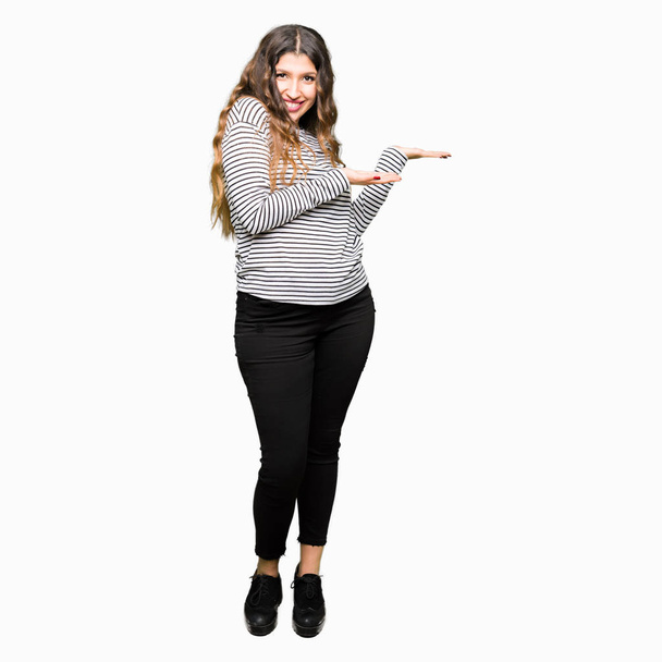 Νεαρή όμορφη γυναίκα που φορούσε ριγέ πουλόβερ τοποθετώντας το δείκτη στην πλευρά με το χέρι και την ανοιχτή παλάμη, παρουσιάζει διαφήμιση χαμογελά ευτυχισμένη και σίγουρη - Φωτογραφία, εικόνα