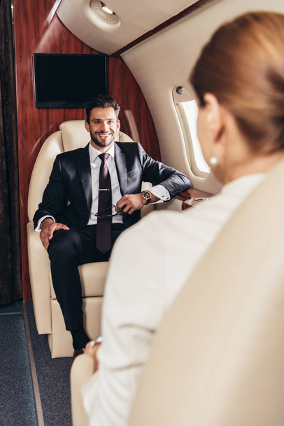 selektywne skupienie się uśmiechniętego biznesmena patrzącego na bizneswoman w prywatnym samolocie  - Zdjęcie, obraz