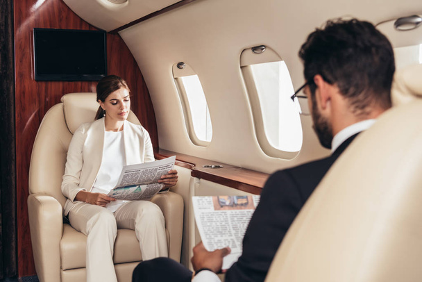 selective focus of businessman and businesswoman reading newspaper in private plane  - Fotografie, Obrázek