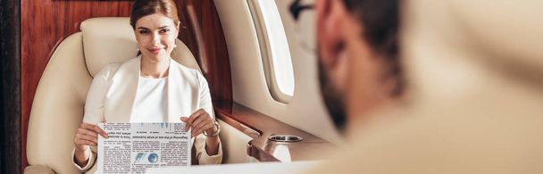 panoramic shot of smiling businesswoman holding newspaper in private plane  - 写真・画像