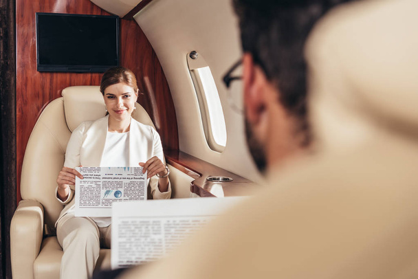 selektywne skupienie się uśmiechniętej bizneswoman trzymającej gazetę w prywatnym samolocie  - Zdjęcie, obraz