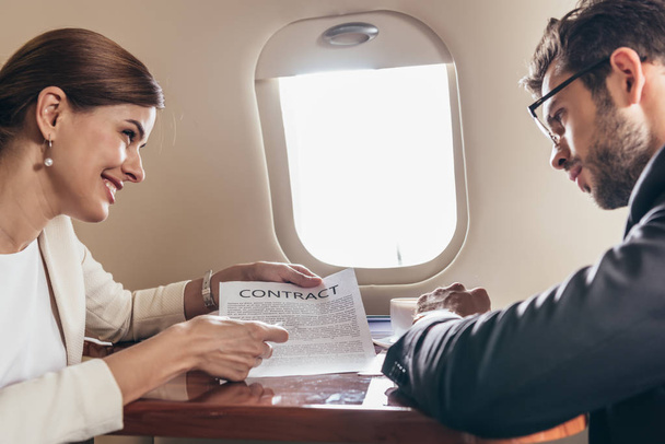 businessman and smiling businesswoman looking at contract in private plane  - Photo, Image