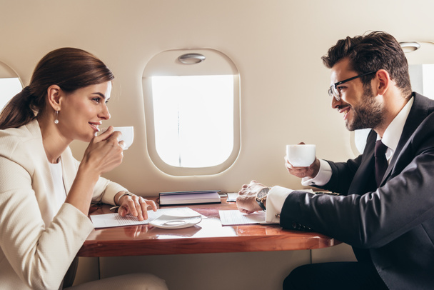 glimlachende zakenman en zakenvrouw drinken koffie in prive-vliegtuig  - Foto, afbeelding