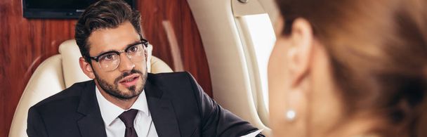 panoramic shot of businessman looking at businesswoman in private plane  - Zdjęcie, obraz