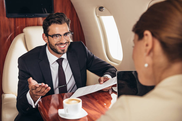 Gülümseyen işadamlarının seçici odak noktası iş kadınlarına bakmak ve özel uçakta kağıt tutmaktır.  - Fotoğraf, Görsel