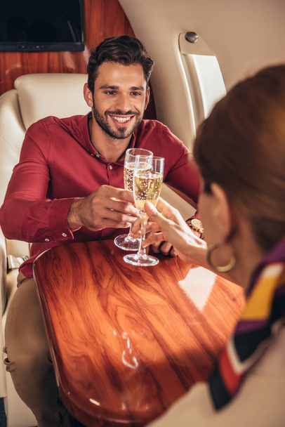 smiling boyfriend and girlfriend clinking with champagne glasses in private plane  - Photo, Image