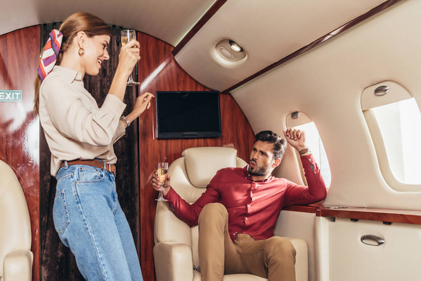 fidanzato sorridente e fidanzata che tiene bicchieri di champagne in aereo privato
  - Foto, immagini