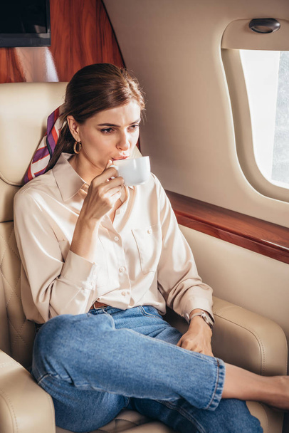 プライベート飛行機でコーヒーを飲むシャツの魅力的な女性  - 写真・画像