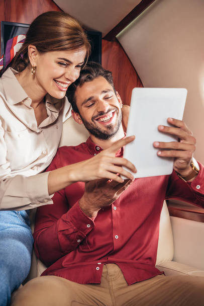 smiling boyfriend and girlfriend holding digital tablet in private plane  - Foto, afbeelding
