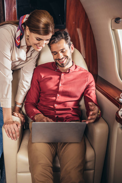 smiling boyfriend and girlfriend looking at laptop in private plane  - Foto, afbeelding