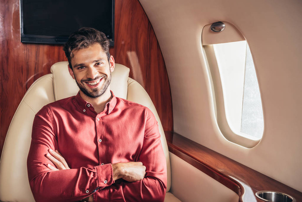 handsome and smiling man in shirt with crossed arms in private plane  - Valokuva, kuva