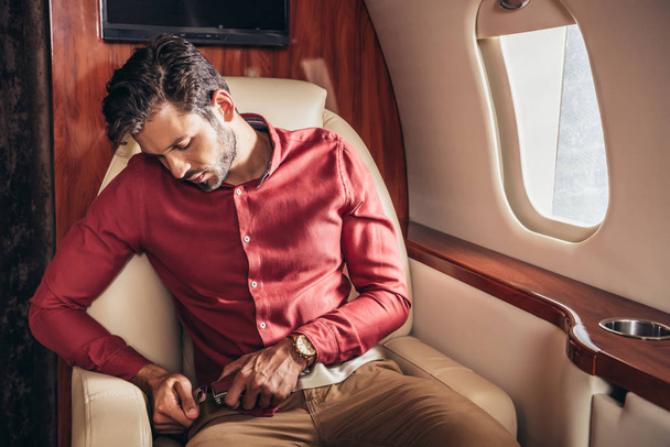 handsome man in shirt putting on seat belt in private plane  - Foto, immagini