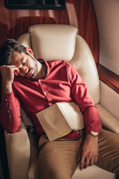 handsome man in shirt sleeping with book in private plane  - 写真・画像