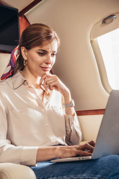 atrakcyjna kobieta w koszuli za pomocą laptopa w prywatnym samolocie  - Zdjęcie, obraz