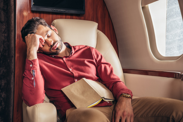 handsome man in shirt sleeping with book in private plane  - Фото, изображение