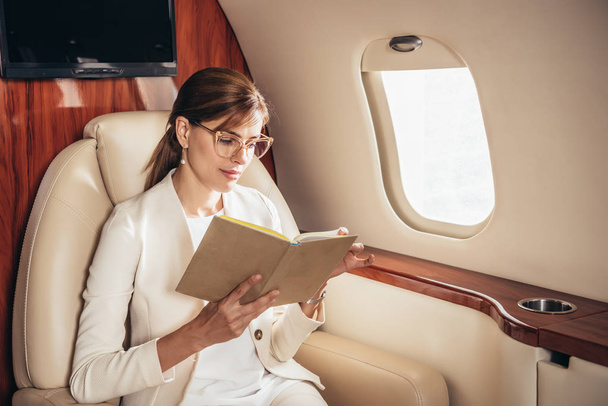 attractive businesswoman in suit reading book in private plane  - Zdjęcie, obraz