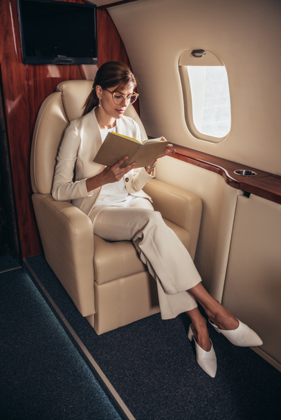 aantrekkelijke zakenvrouw in pak leesboek in prive-vliegtuig  - Foto, afbeelding