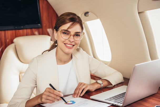 sonriente mujer de negocios en traje haciendo papeleo en avión privado
  - Foto, Imagen