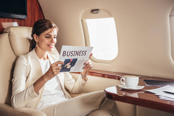 sonriente mujer de negocios en traje leyendo negocios de periódicos en avión privado
  - Foto, imagen