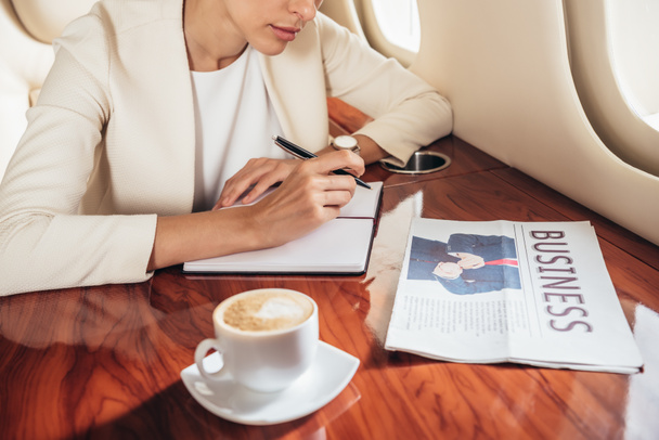 vista recortada de la mujer de negocios en traje escrito en cuaderno en avión privado
  - Foto, imagen
