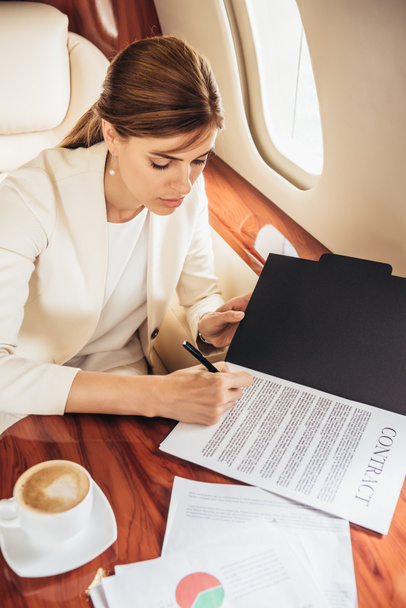 Blickwinkel der attraktiven Geschäftsfrau im Anzug bei der Vertragsunterzeichnung im Privatflugzeug  - Foto, Bild