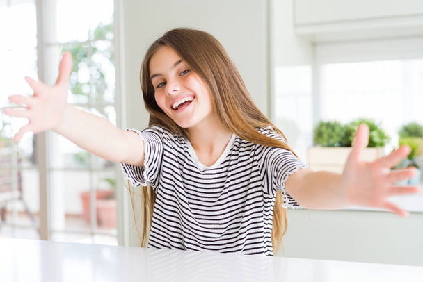 Beautiful young girl kid wearing stripes t-shirt looking at the camera smiling with open arms for hug. Cheerful expression embracing happiness. - Foto, Bild