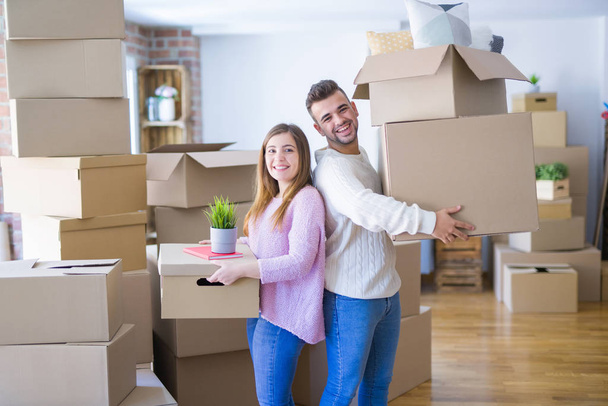 Young beautiful couple in love moving to new home, holding cardboard boxes very happy and cheerful for new apartment - Photo, Image