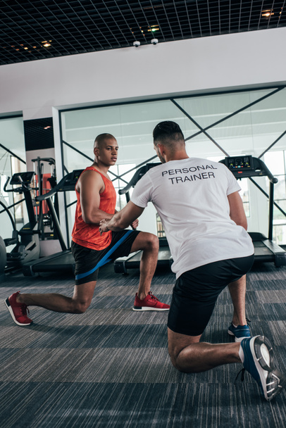 visão traseira do personal trainer instruindo esportista afro-americano exercitando com expansor
 - Foto, Imagem