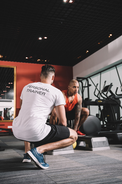 back view of personal trainer supervising african american athlete lifting weight in gym - Fotografie, Obrázek