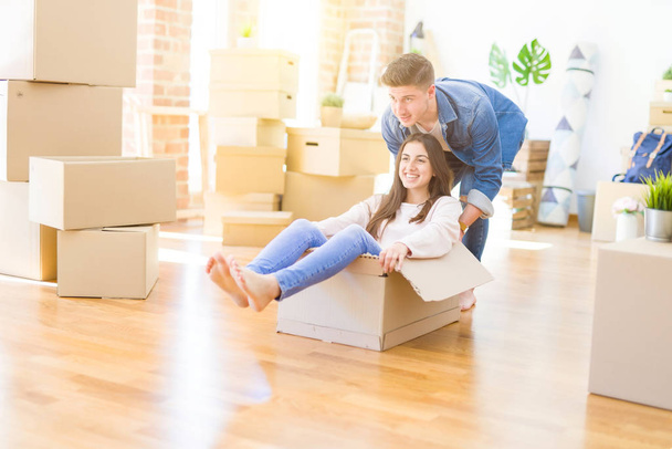Beautiful young couple smiling in love having fun riding inside a cardboard box, celebrating moving to a new home - Photo, Image