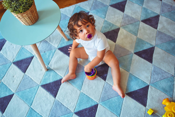 Όμορφο μικρό παιδί κορίτσι χρησιμοποιώντας πιπίλα παίζει με τα παιχνίδια στο χαλί - Φωτογραφία, εικόνα