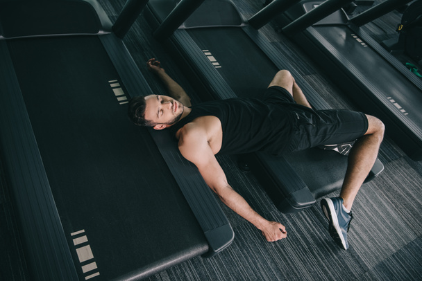 top view of unconscious sportsman lying on treadmill in gym  - Fotoğraf, Görsel