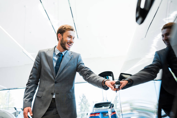 selectieve focus van gelukkige man openen autodeur in auto showroom  - Foto, afbeelding
