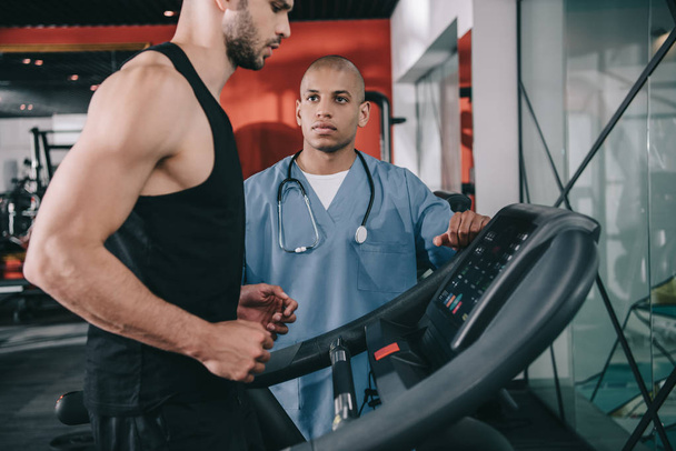 young african ameriican doctor supervising sportsman running on treadmill - Foto, Bild