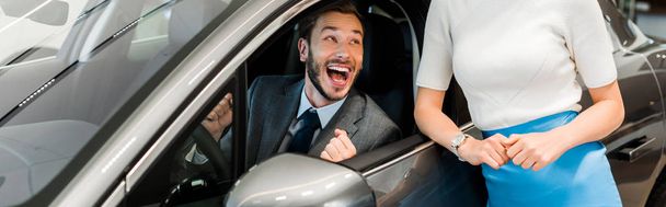 panoramic shot of woman standing near excited bearded man in car  - Foto, immagini