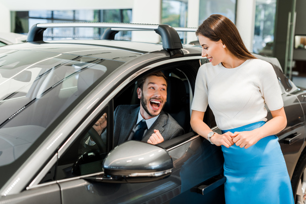 atrakcyjna kobieta stoi w pobliżu podekscytowany mężczyzna w samochodzie  - Zdjęcie, obraz