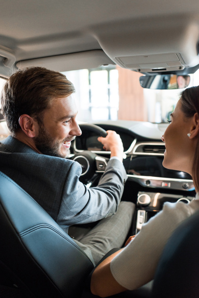 selective focus of happy bearded man holding steering wheel and looking at woman in car  - Photo, Image
