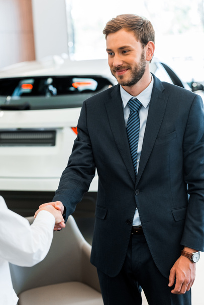 cropped view of woman shaking hands with happy car dealer in car showroom  - Foto, afbeelding