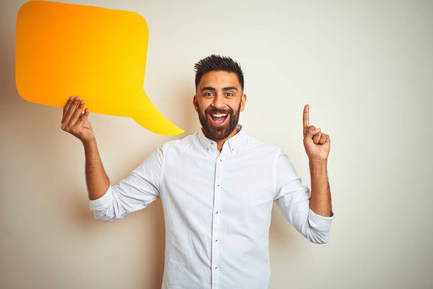 Young arab indian hispanic man holding speech bubble over isolated white background surprised with an idea or question pointing finger with happy face, number one - Foto, Imagen