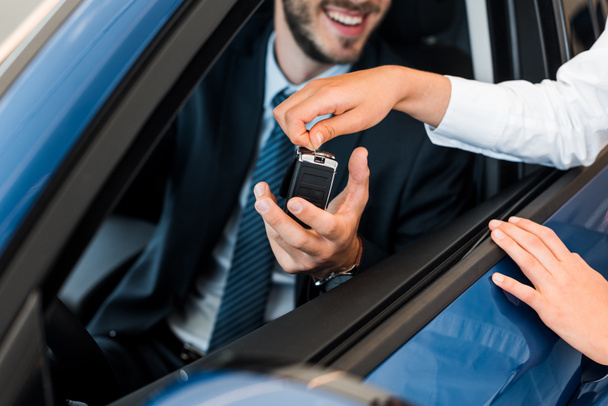 cropped view of car dealer giving car key to bearded man  - Zdjęcie, obraz