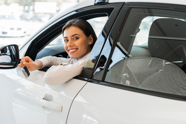 χαρούμενη νεαρή γυναίκα κρατώντας το κλειδί του αυτοκινήτου, ενώ κάθεται στο αυτοκίνητο  - Φωτογραφία, εικόνα