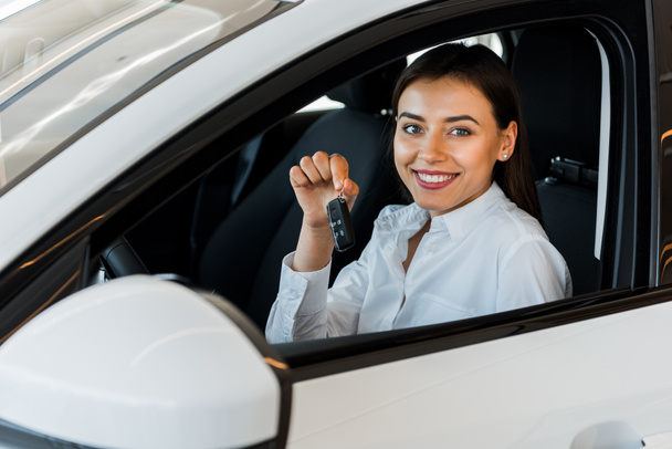 selective focus of happy woman holding car key while sitting in car  - Foto, imagen