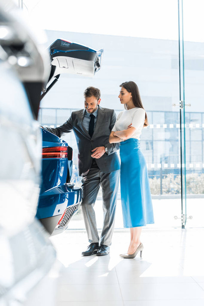 selective focus of happy woman and man looking at car trunk in car showroom  - Foto, imagen