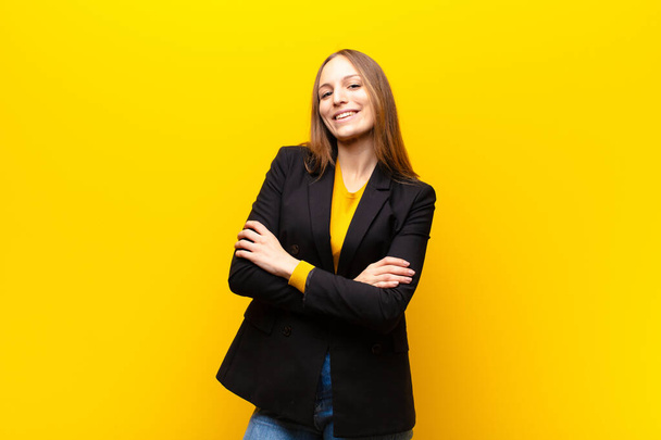 young pretty businesswoman laughing happily with arms crossed, with a relaxed, positive and satisfied pose against orange background - Foto, Imagen