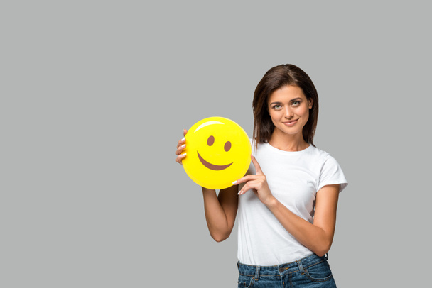 Κίεβο, Ουκρανία - 10 Σεπτεμβρίου 2019: χαρούμενη γυναίκα που κρατάει κίτρινο χαμογελαστό emoji, απομονωμένη στο γκρι - Φωτογραφία, εικόνα