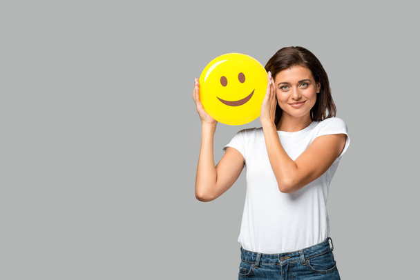 KYIV, UKRAINE - SEPTEMBER 10, 2019: happy young woman holding yellow smiling emoji, isolated on grey - 写真・画像