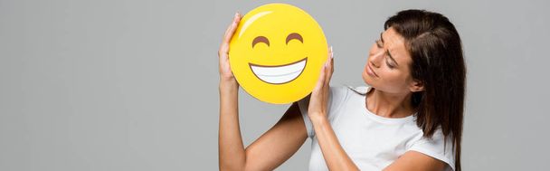 kyiv, ukraine - 10. September 2019: brünette Frau mit gelbem glücklich lächelndem Emoji, isoliert auf grau - Foto, Bild