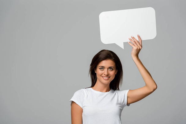 cheerful woman holding empty speech bubble, isolated on grey - Фото, изображение